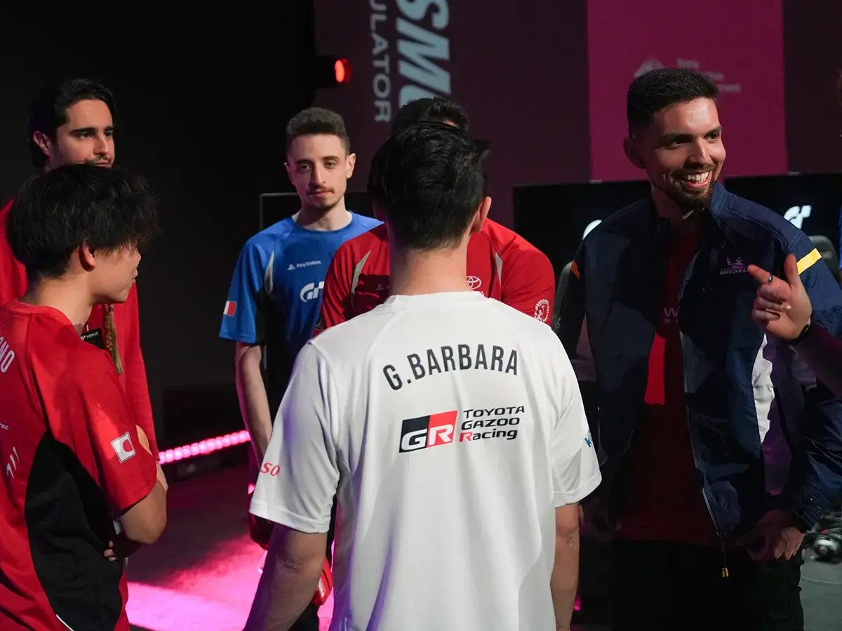 A group of esports players in red, blue, and white Toyota Gazoo Racing shirts stands together, smiling and engaged in conversation