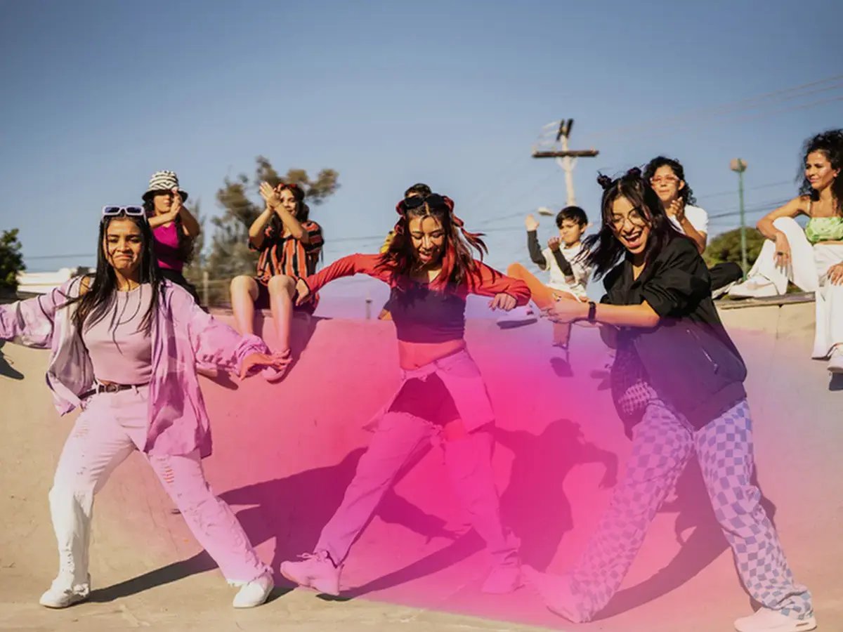 A group of people enjoys dancing in a skate park bathed in warm sunlight
