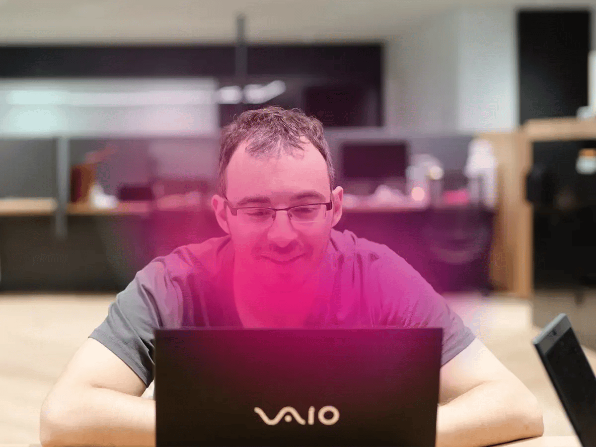A man in glasses works on a Vaio laptop in an office, illuminated by pink light