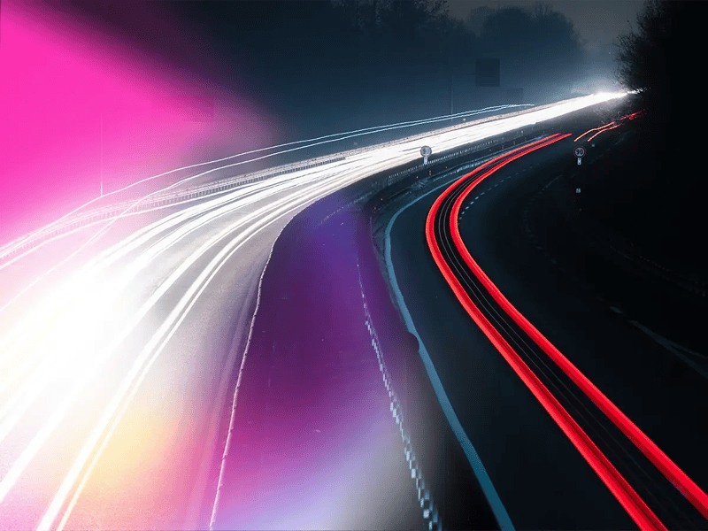 A nighttime highway scene with vibrant light trails showing motion
