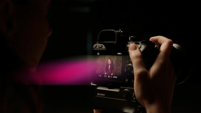 A person holds a Sony camera, focusing on the digital screen displaying a woman posing against a dark background