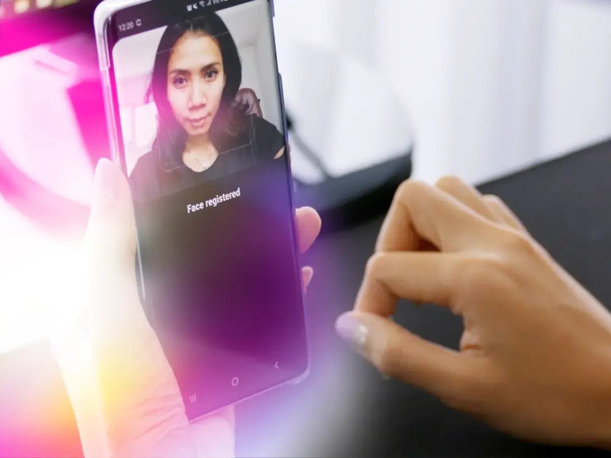 A person holds a smartphone displaying facial recognition with Face registered text