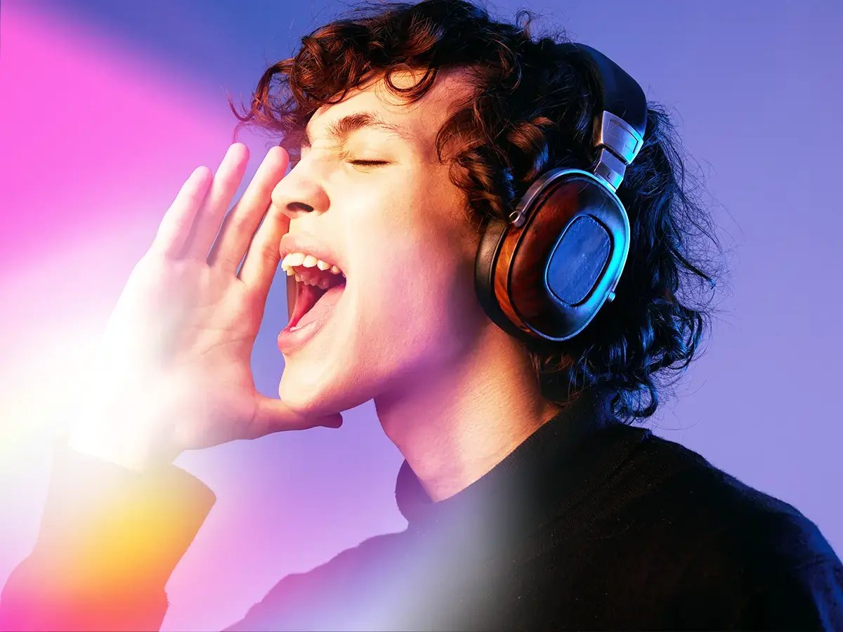 A person joyfully singing with headphones on, eyes closed, and hand near their mouth