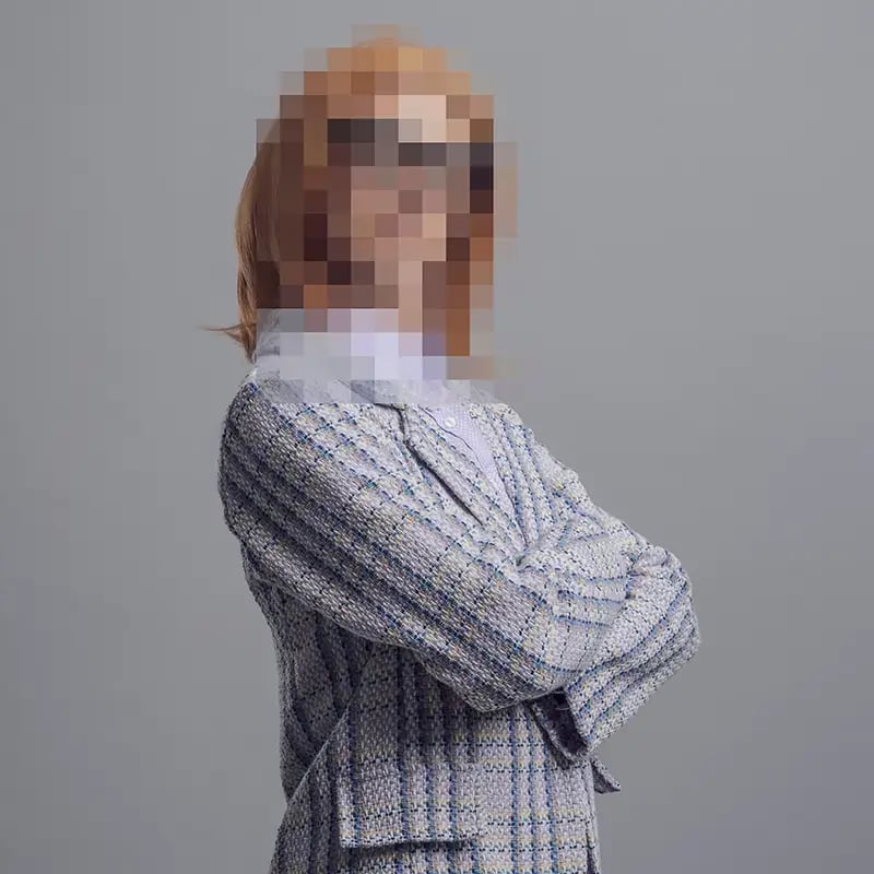 A person stands confidently with crossed arms, wearing a checkered blazer