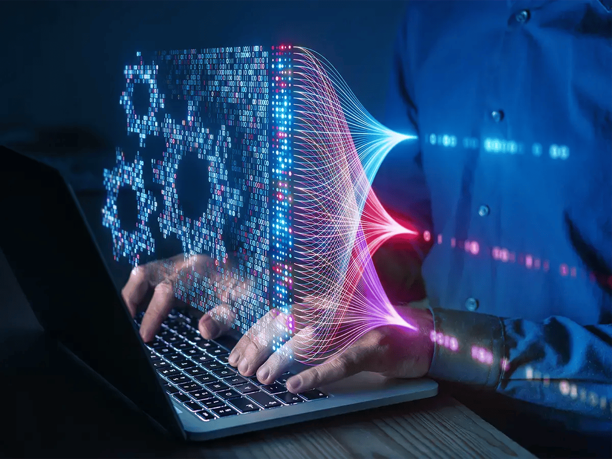 A person types on a laptop, with digital gears and flow lines emerging