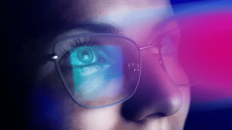 Close-up of a person wearing glasses with a blue digital screen light reflecting on the lenses