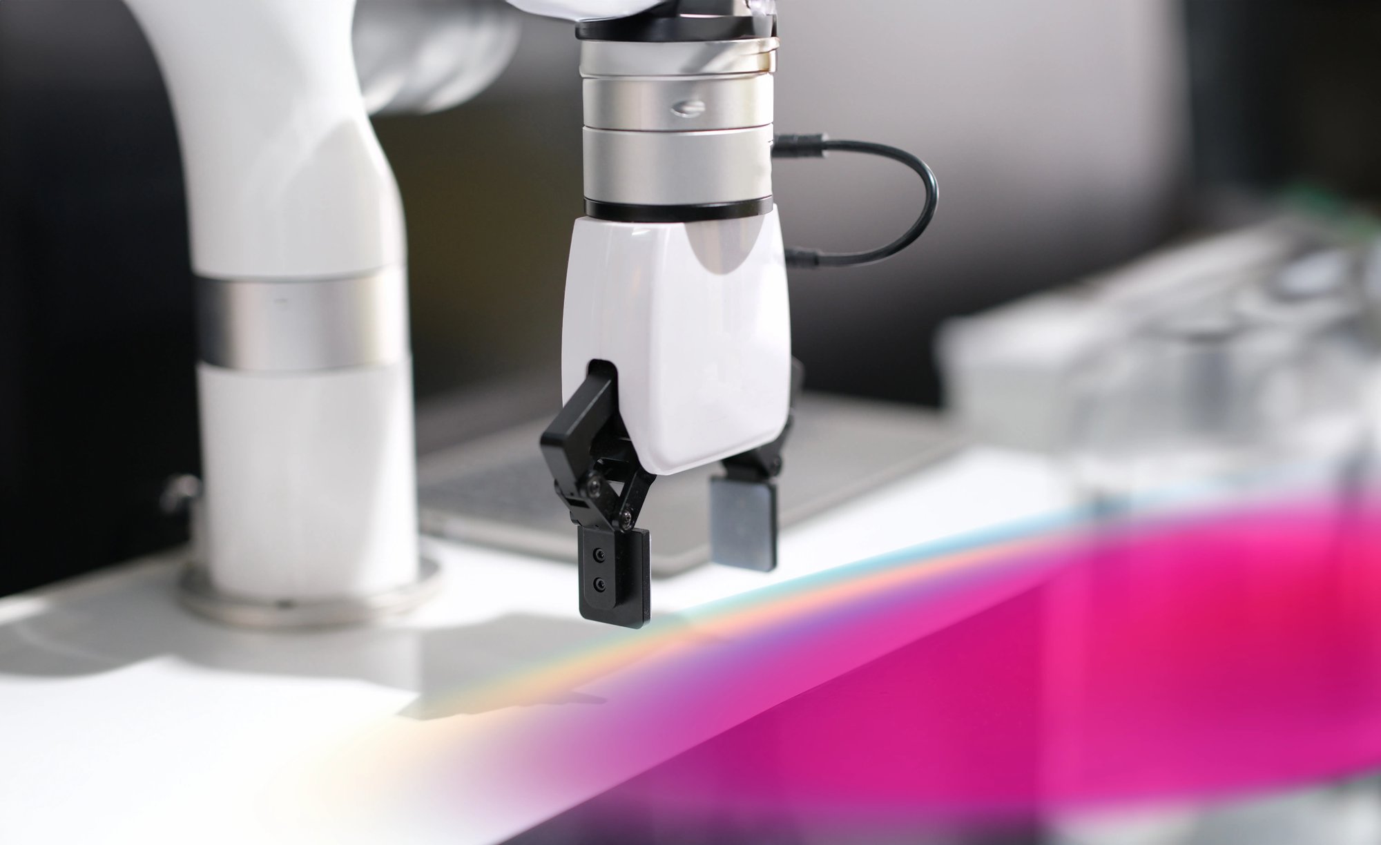 Close-up of a robotic arm with a two-pronged gripper hovering above a smooth, white surface in a modern, industrial setting