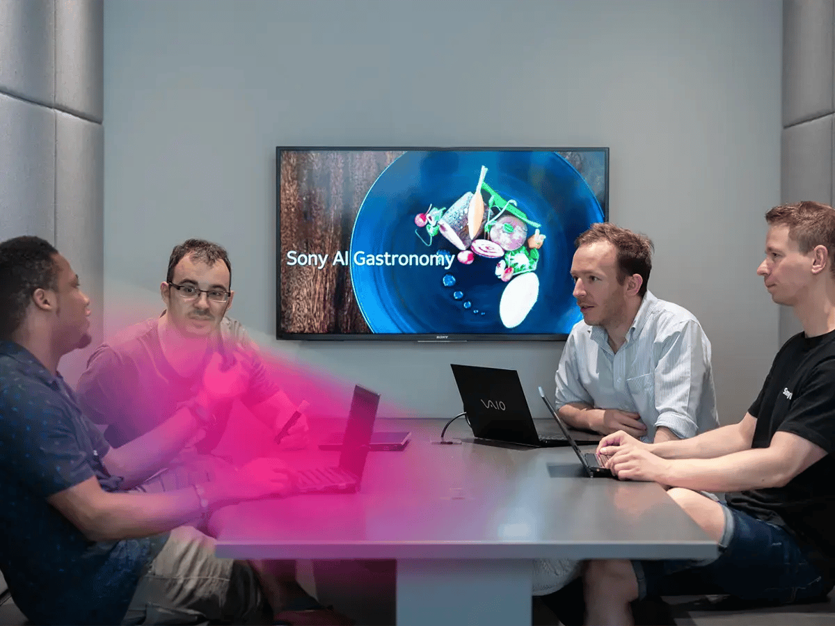 Four people are discussing in a meeting room with laptops, focusing on a screen displaying Sony AI Gastronomy and an image of a dish