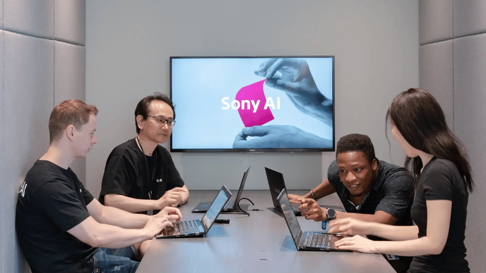 Four people collaborate at a table with laptops in a modern room