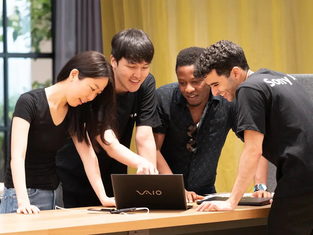 Four people gather around a laptop, smiling and engaged