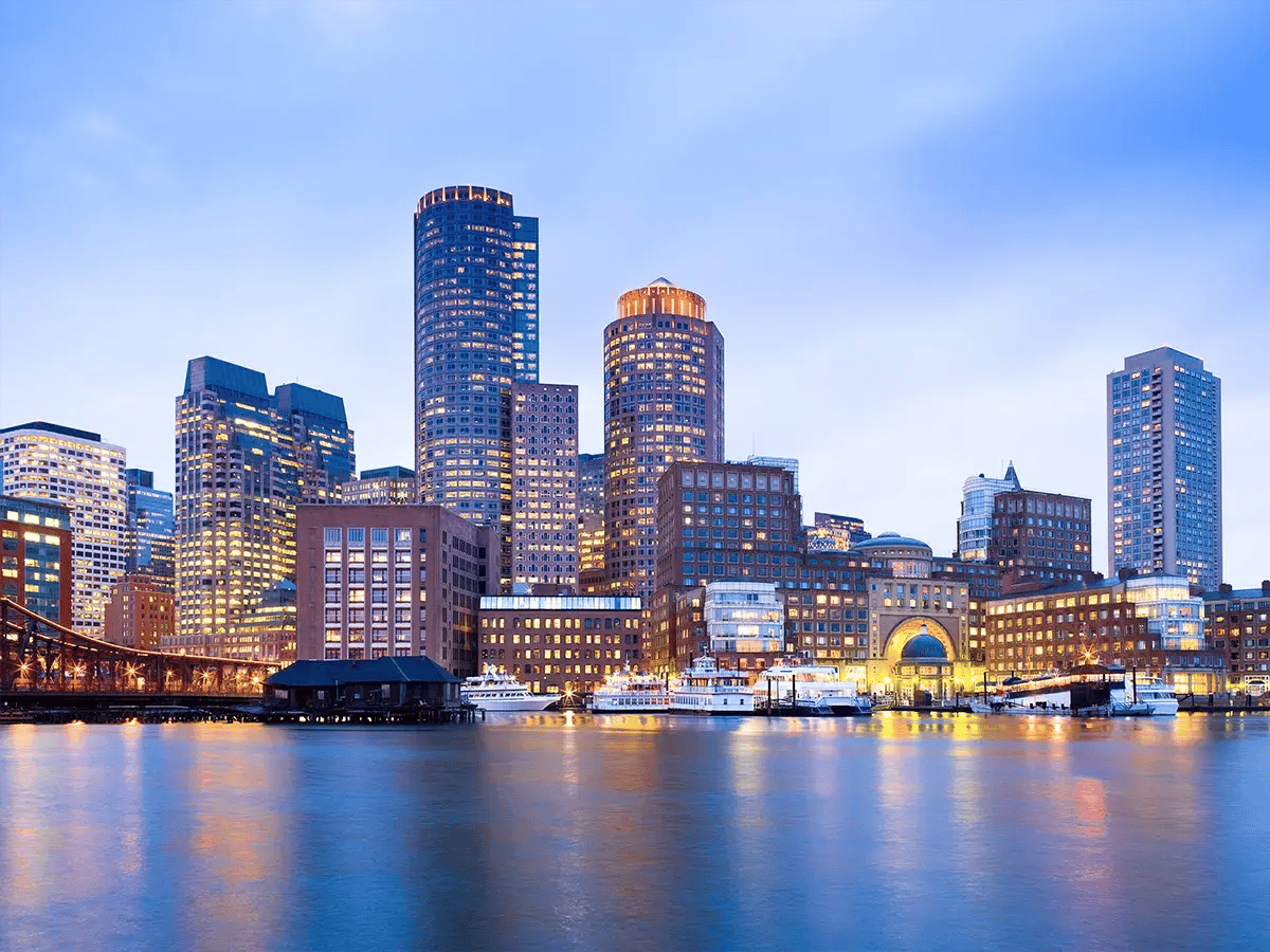 Skyline of Boston at dusk with illuminated skyscrapers reflecting on the harbor