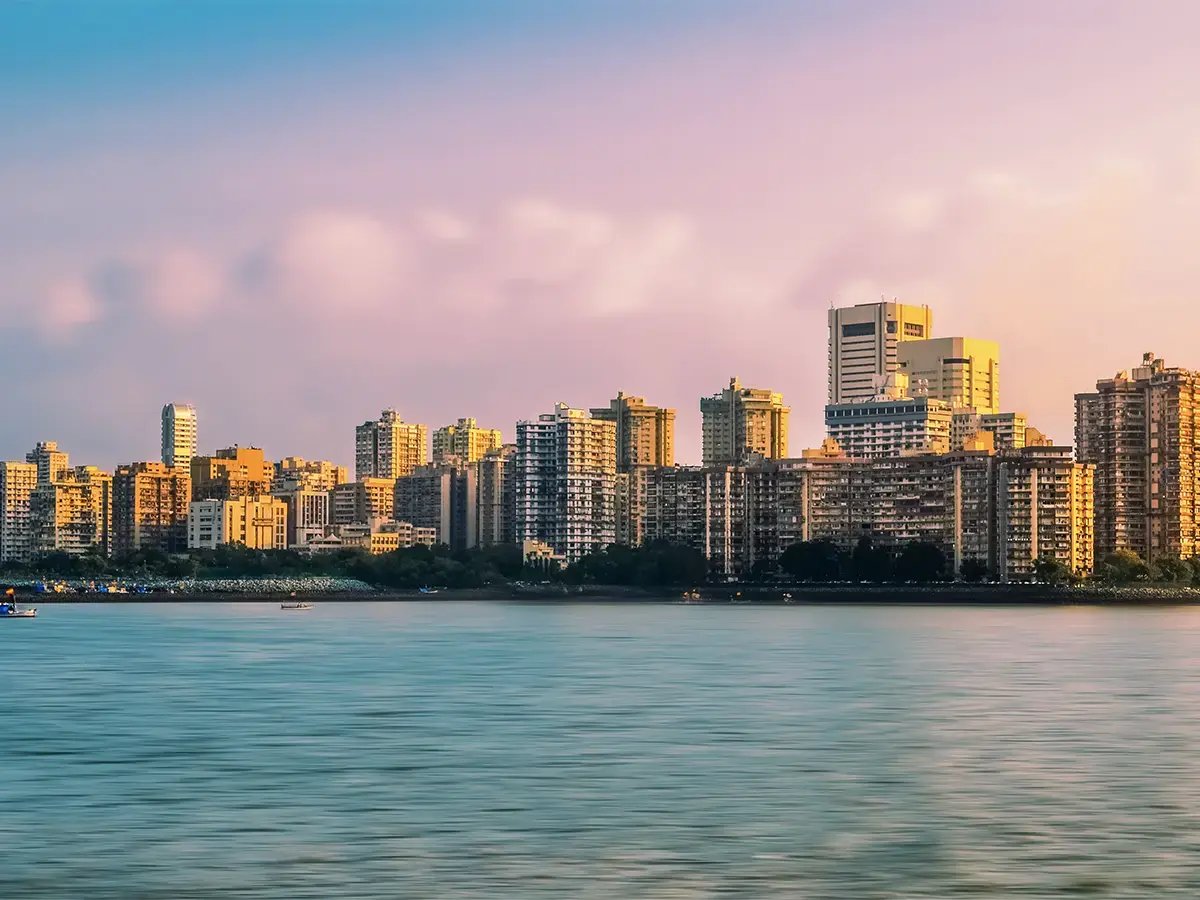 Skyline of Mumbai with tall buildings at sunset, their reflections shimmer in calm waters