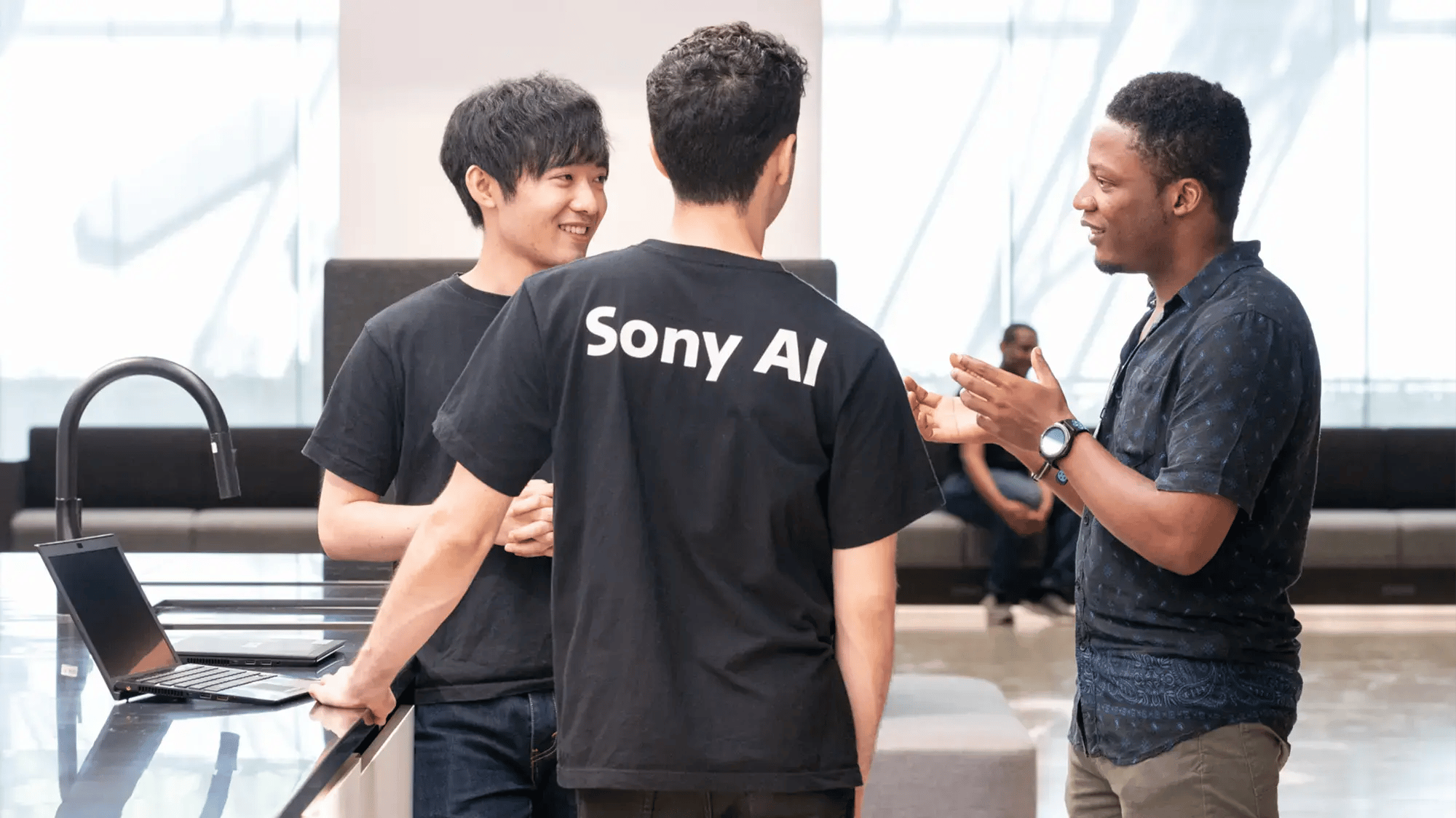 Three people engage in a discussion around a laptop in a modern office