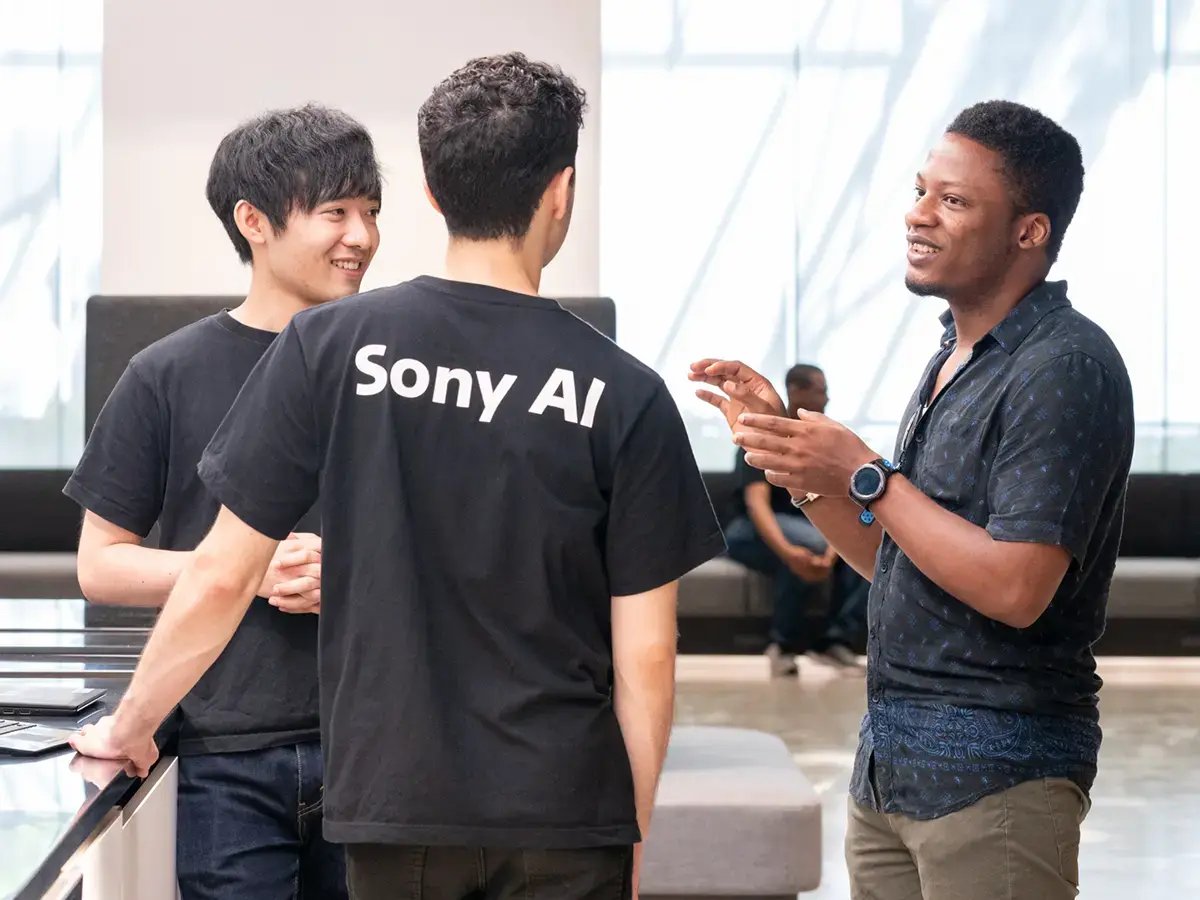 Three people in casual attire are engaged in a lively discussion in a bright, modern space